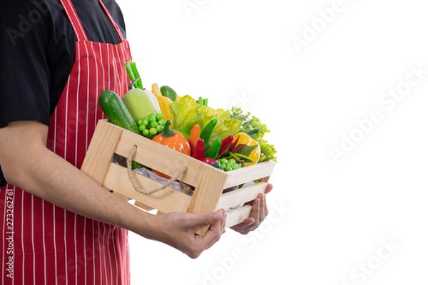 Fototapeta An asian male wearing red apron carry a basket of fully vegetable and fruit isolated on white background with clipping path. Concept of deliver, cook healthy fresh food from farm to kitchen market 