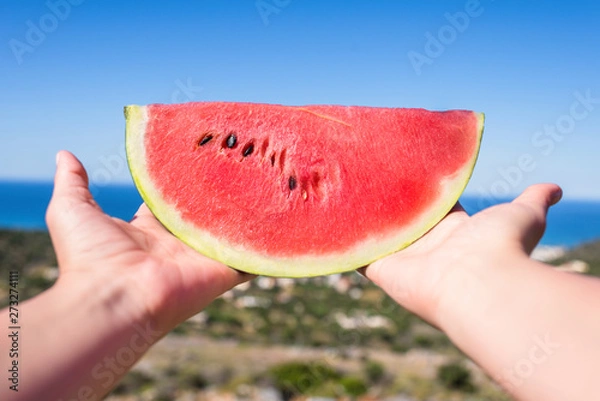 Fototapeta Ripe piece of watermelon in female hands on the background of the sea on a hot summer day. Concept