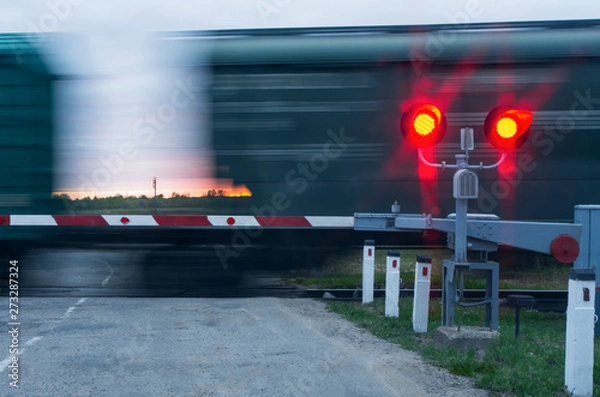 Fototapeta Two traffic lights with red light and barrier in the background moving wagons and sunset