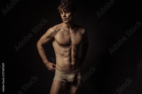 Obraz Strong stripped muscle male model in beige underwear on black isolated font background