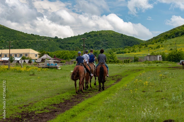 Obraz Four people on horses against the backdrop of highlands and beautiful cloudy sky.