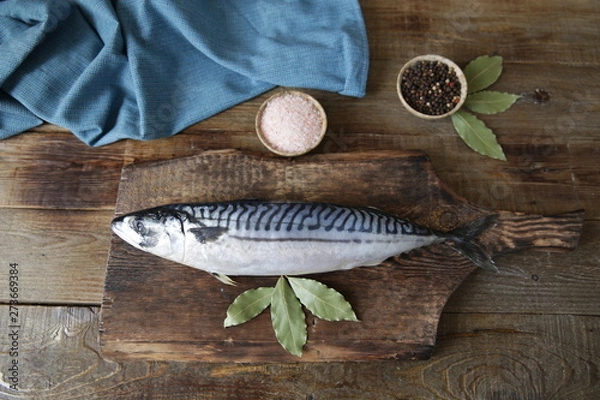 Fototapeta Fresh mackerel with salt, pepper and bay leaves on a wooden cutting board and wooden rustic background with copy space for text. Flat lay. Top view. 