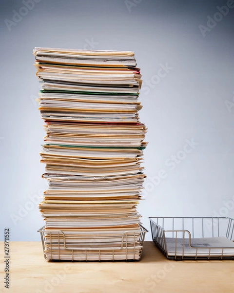 Obraz In, out trays on desk with tall stack of never ending office paperwork