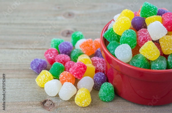 Obraz small red bowl overflowing with brightly colored candy gumdrops on a wood background with copy space