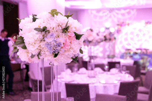 Obraz Beautiful table setting with crockery and white flower arrangements in a vase on a high stem for a party, wedding reception or other festive event. Glassware and cutlery for catered event dinner