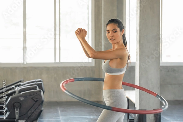 Fototapeta attractive sport asia woman rotates hula hoop in sport gym