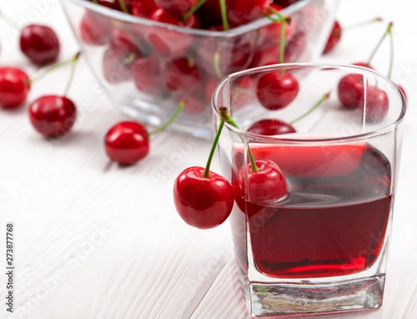 Fototapeta A lot of red, ripe cherries with a glass of cherry juice on a white background