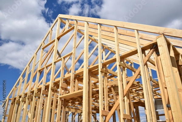 Obraz Wood frame residential building under construction.Building construction, wood framing structure at new property development site.new home currently under construction against blue sky.mortgage, loan.