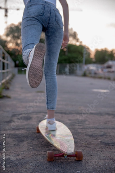 Obraz A girl pushes off with her foot and rolls on a longboard.