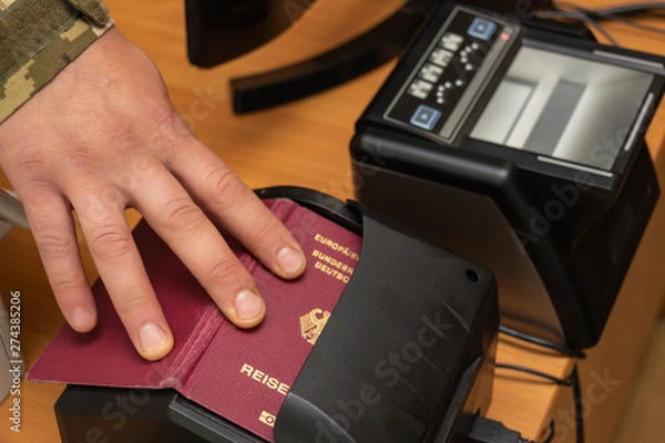 Fototapeta The process of scanning a German biometric passport to register the fact of crossing the state border. Male hand applies a passport to the scanning device. Concept of overseas travel