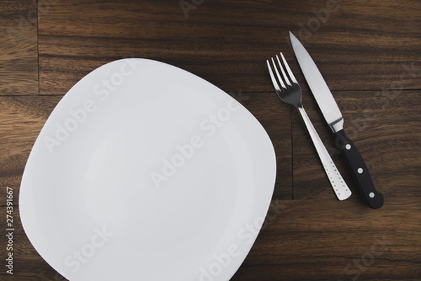 Obraz Empty white plate, spoon and knife isolated on wooden background. diet concept.