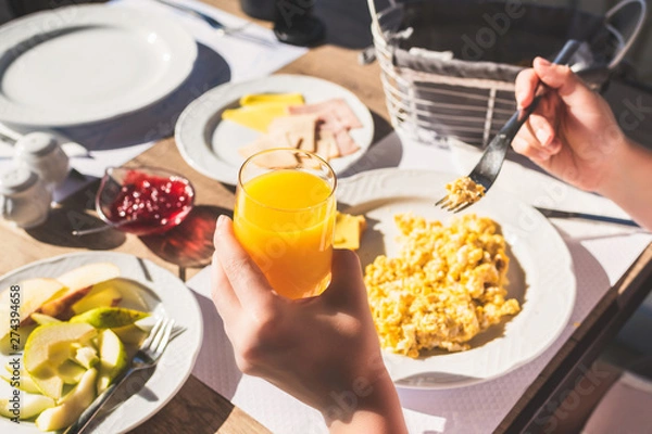 Fototapeta Woman have a breakfast with scrambled eggs, fresh orange  juice ham, cheese, bread and jam in a hotel restaurant.