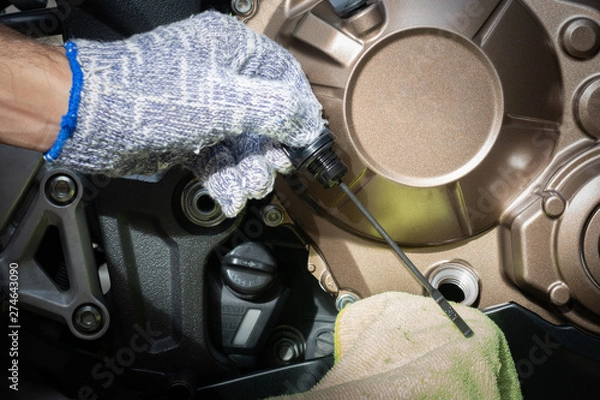 Obraz Hand of technician wearing cloth gloves check lubricant engine oil level motorcycle bigbike. maintenance motorcycle concept in garage or check before you travel.