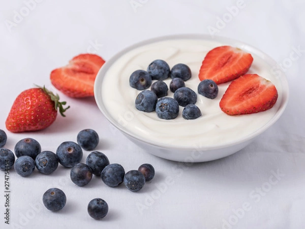 Obraz White yogurt in bowl with strawberries, blueberries on the top on white background.