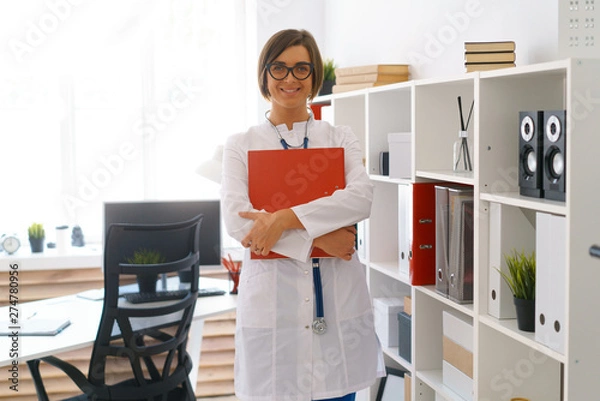 Obraz young beautiful doctor in white gown stay in her consulting room wait for patients hold binder study database of case histories