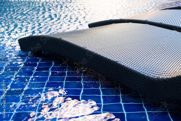 Obraz close up rattan pool chair beside the swimming pool with the blue water and sun light reflection