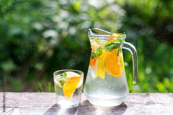 Fototapeta fresh lemonade with orange and a glass on wooden old table against a backdrop of green grass
