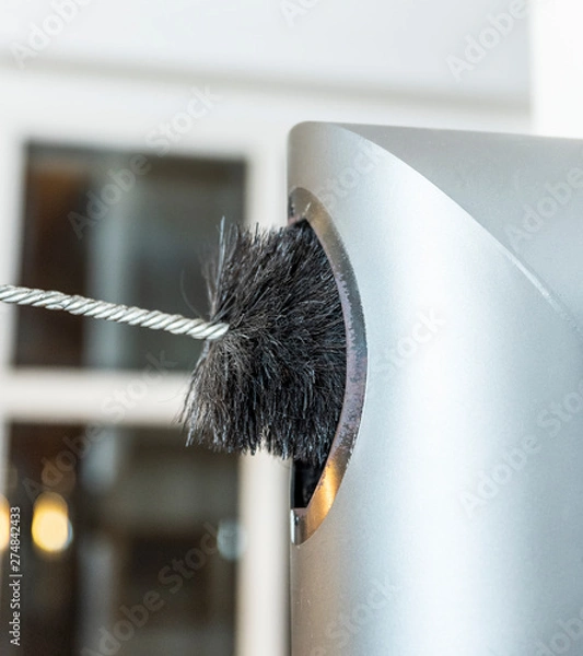 Obraz Chimney sweep cleaning a chimney standing balanced on the apex of a house roof lowering equipment down the flue