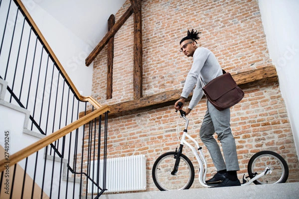 Obraz Young mixed race businessman with scooter in office building.