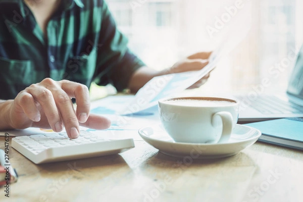 Obraz The accountant is pressing the calculator to calculating check the accuracy of the investment budget with using computer laptop and document data to analysis.