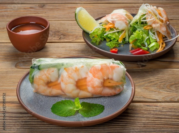 Fototapeta Close Up view of Vietnamese spring rolls with shrimps on two plates on wooden background. Soft focus.
