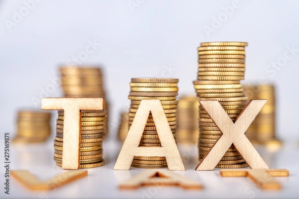 Obraz Bars stacked from coins on a white table. TAX and VAT lettering with wooden letters based on coins. White background.