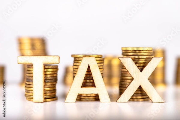 Fototapeta Bars stacked from coins on a white table. TAX lettering with wooden letters based on coins.