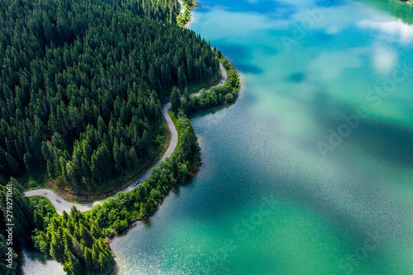 Fototapeta Aerial view over beautiful turquoise mountain lake and green forest. Spring in the mountains. Green forest, mountain lake. Green pine and fir trees forest and a lake. Beautiful mountain road. - Image