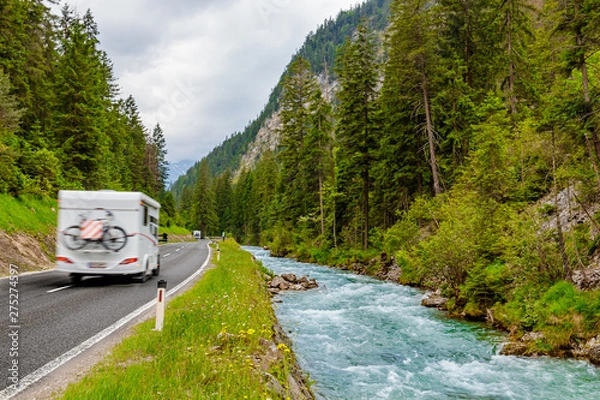Fototapeta Camper van with attached bicycle driving through the European Alps on a rainy day.