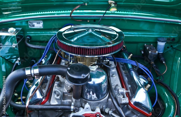 Obraz Classic muscle car engine close up view. Clean, shiny surface. Silver, chrome, red, blue and green colored part elements. Big round air intake with filter. Lots of tubes, wires, pipes, devices inside.