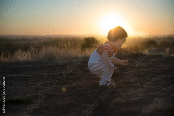 Fototapeta Sunny evening and the first independent steps. Baby's first steps in nature