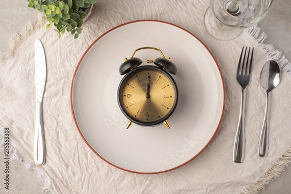 Fototapeta a plate with an alarm clock at which time is 12am, concept lunch time
