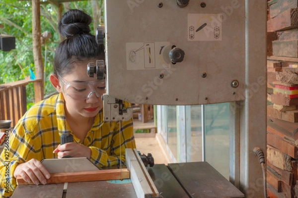 Fototapeta Women standing is craft working cut wood at a work bench