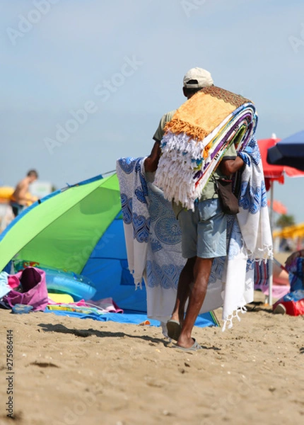 Fototapeta abusive itinerant seller on the sand while selling towels and be