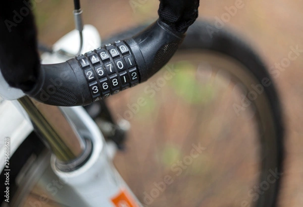 Obraz Cable for attaching a bicycle with a combination lock hanging on the handlebars with a blurred wheel background.