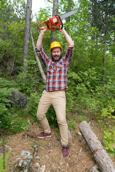 Fototapeta bearded lumberjack with a chainsaw makes faces