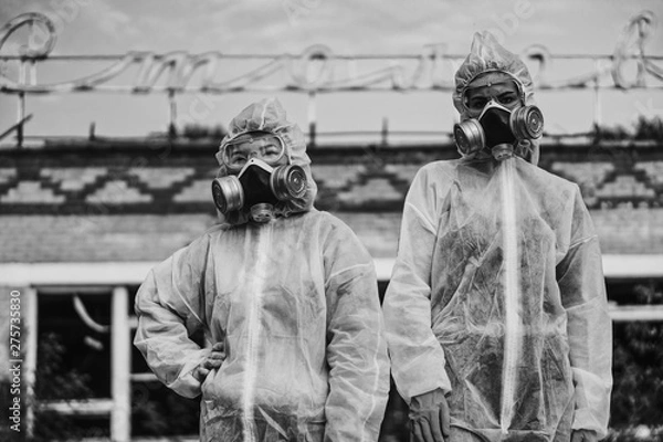 Fototapeta Two scientists put on a respirator and a radiation protective suit. Stern look into the camera from the abandoned territory. Care about ecology in black and white photo mystical horror movie.