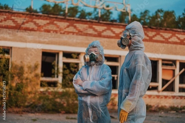 Fototapeta Two scientists put on a respirator and a radiation protective suit. Stern look into the camera from the abandoned territory. Care about ecology in bright saturated photos.