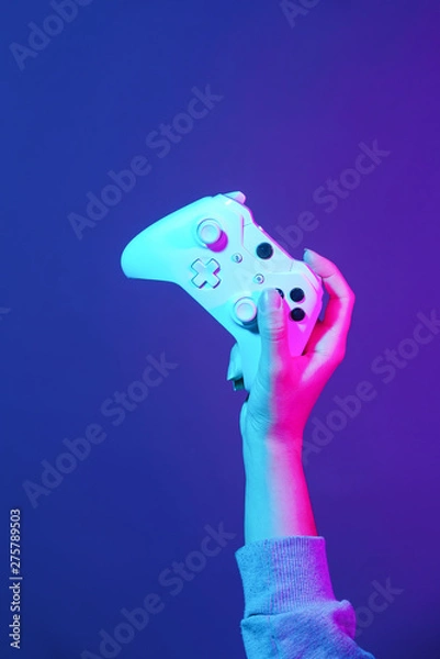 Fototapeta Hand with white gamepad on dark violet background.
