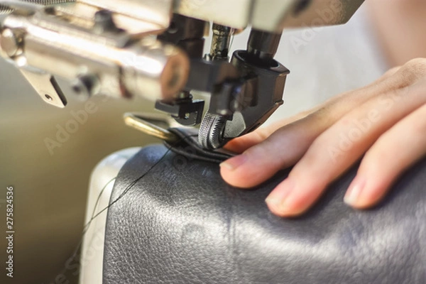 Fototapeta Sewing machine in a leather workshop in action with hands working with a leather details