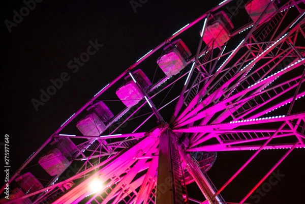Fototapeta Close up of a bright pink ferris wheel lit up against a dark sky during a festival in a city