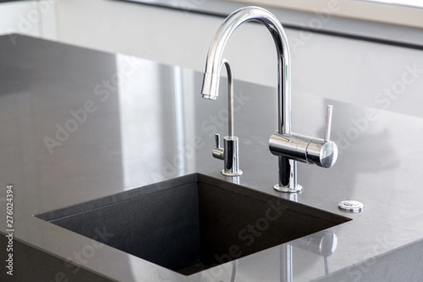 Obraz kitchen sink of dark gray stone with chrome faucet in a clean kitchen with a glossy work surface, close up faucet sink.