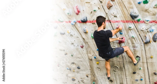 Fototapeta Man practicing rock climbing on artificial wall indoors. Active lifestyle and bouldering concept with copy space.