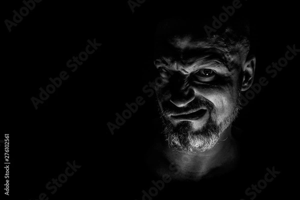 Fototapeta  Face with a bearded man grimace against a dark background with sharp shadows. Comedic, fabulous villain or negative character conception with copy space.