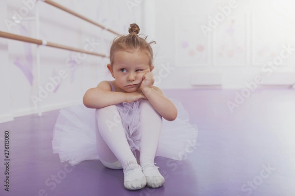 Obraz Adorable little girl ballerina looking grumpy, sitting alone on the floor at ballet school, copy space. Cute little ballerina looking bored and annoyed at ballet dancing class