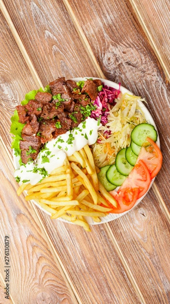 Fototapeta Shawarma plate with beef, french fries, vegetables and sauce close-up on a wooden table. vertical top view from above. Flat lay