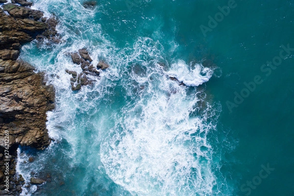 Fototapeta Aerial drone view of ocean's beautiful waves crashing on the rocky island coast