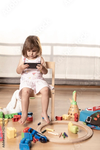Fototapeta Girl Plays Mobile Phone. The Girl is Hooked to the Mobile Phone. He does not play with toys. The mobile phone is bad for children.