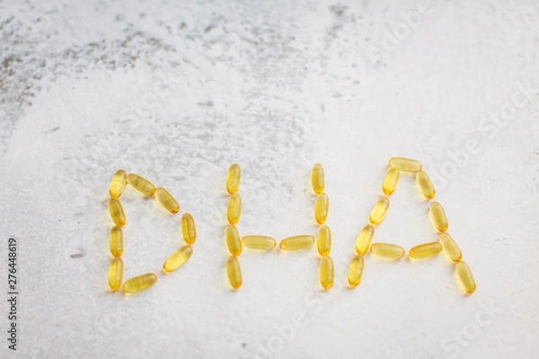 Obraz capsules laid out in the form of letters DHA. Close up gold capsules of omega-3 .