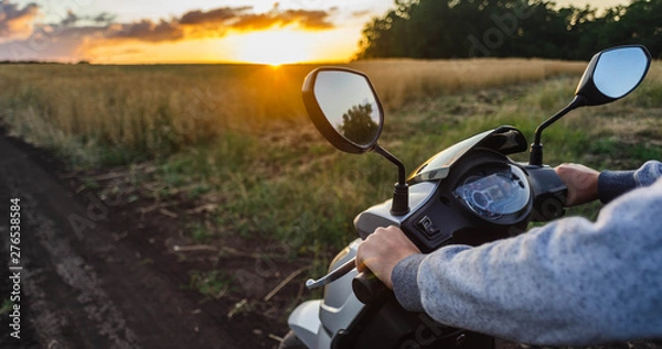 Fototapeta Riding along an empty road in the forest against the sunset sky. Scooter steering wheel and speedometer closeup. The concept of freedom, high speed and travel in nature, banner.